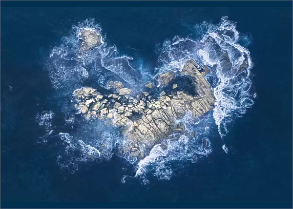 Ocean waves crashing over heart-shaped rock island