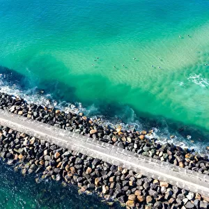 Aerial View of rock walkway out into the ocean with surfers