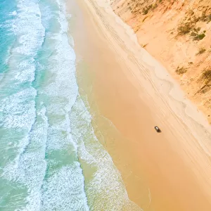 Aerial view of sand dunes with vehicles travelling along the sand and the ocean