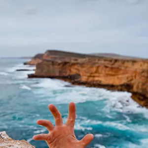 Hands reaching up to grip a cliff. Dangerous ocean in the background