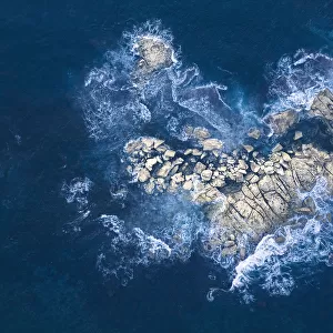 Ocean waves crashing over heart-shaped rock island