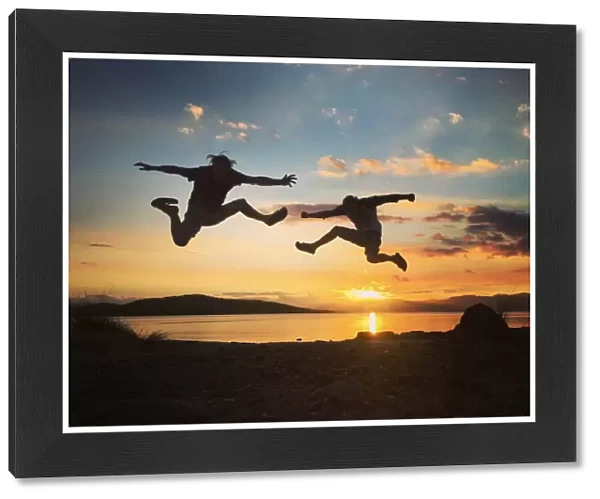 Silhouette of two men jumping into the sunset sky