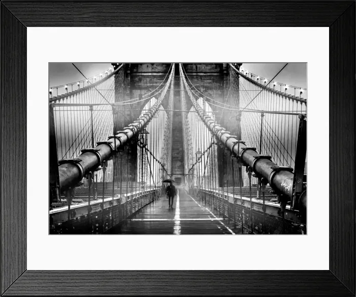 Framed Print : A lone man with umbrella walks along a foggy Brooklyn Bridge at dusk in black and white