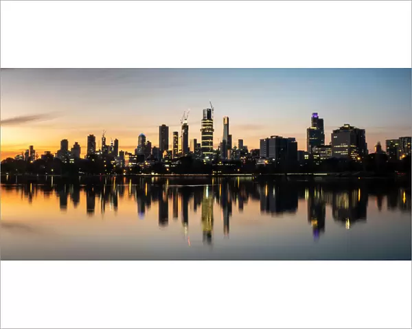 The reflections of the melbourne city skyline at dusk in the still water of albert park