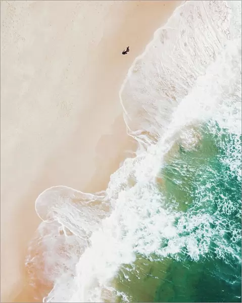 An aerial beach shot of guy walking on the beach and the waves breaking on the shore