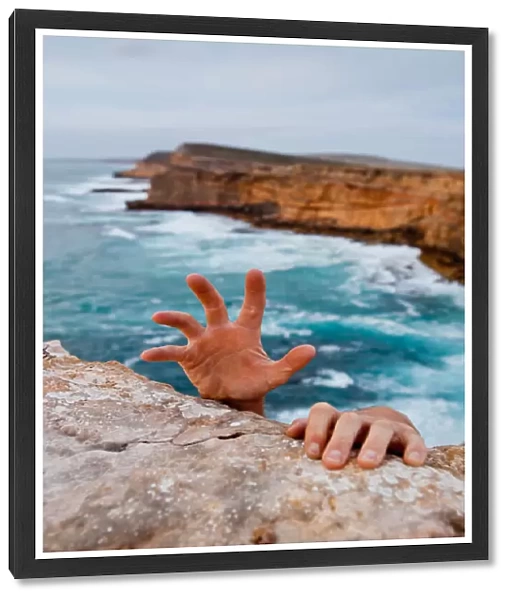 Hands reaching up to grip a cliff. Dangerous ocean in the background