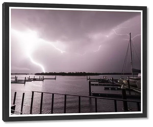 Flashes of bright lightning strikes across the water with boats silhouetted