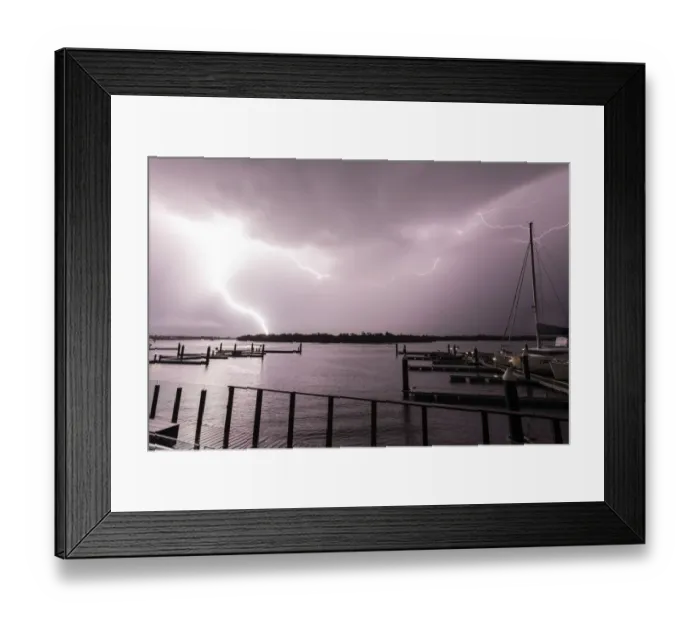 Framed Print : Flashes of bright lightning strikes across the water with boats silhouetted
