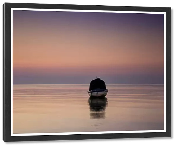 Reflections of a single boat moored on the bay at sunrise in fog, South Werribee