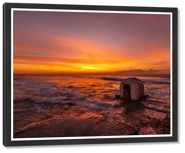 Beautiful red, yellow and orange colors of a sunrise over the ocean with a little concrete hut