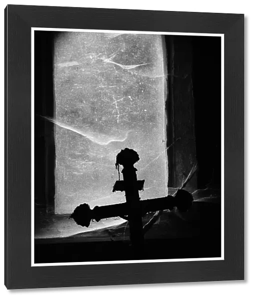 Close-up of a crucifix photographed against the light in front of a window covered by dust and spider webs at the Pere Lachaise cemetery in Paris, France