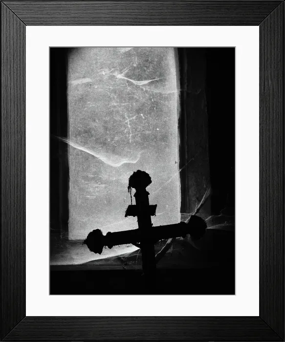 Framed Print : Close-up of a crucifix photographed against the light in front of a window covered by dust and spider webs at the Pere Lachaise cemetery in Paris, France