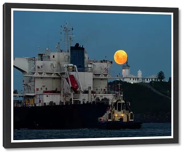 full moon rising above a lighthouse with ship in foreground