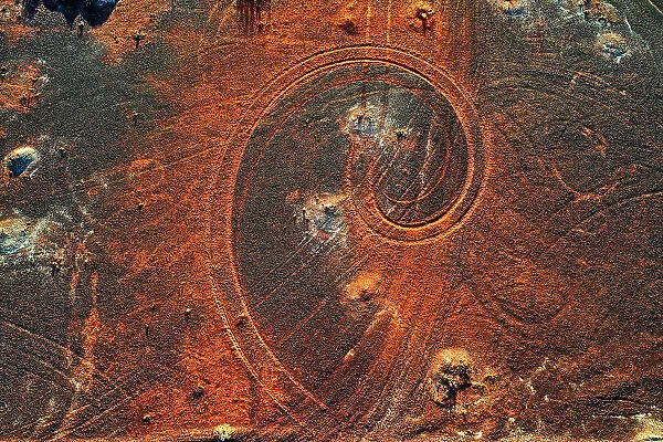 Abstract swirl pattern from car tyre tracks in red dirt, illuminated by dusk sunlight, remote rural Australia