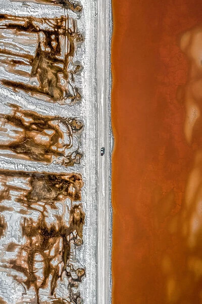 Aerial shot of an dirt track and a truck alongside vibrant coloured salt ponds