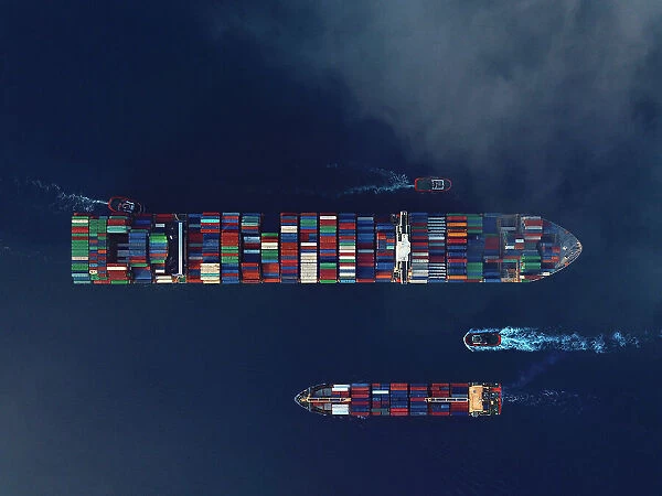 Aerial view of two cargo ships being guided by tugboats. Shipping Container Trading Business