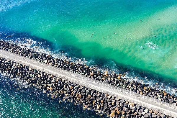 Aerial View of rock walkway out into the ocean with surfers