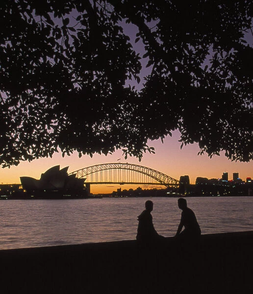 Australia, New South Wales, Sydney, silhouette of couple with Harbour Bridge and Opera house in background at sunset