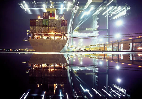 Container ship being loaded by illuminated cranes in dock, night