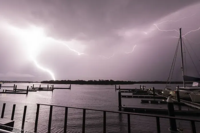 Framed Print : Flashes of bright lightning strikes across the water with boats silhouetted