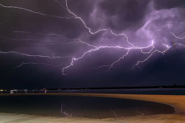 Flashes of bright lightning strikes across the water with stormy clouds and sky
