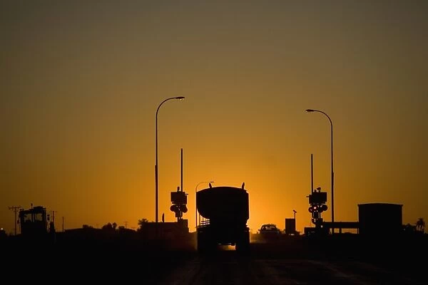 A freight truck and car stopped at a railroad crossing silhouetted against the setting sun