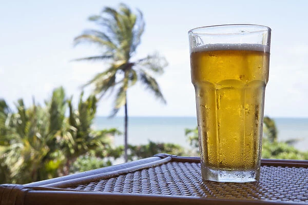 A glass of cold beer on a table with a view of a beach