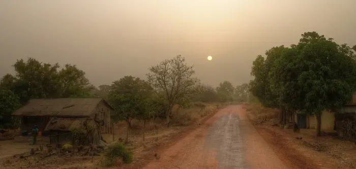 Framed Print : Local road in rural Gambia with farmhouse, forest and sunrise sun on hazy morning