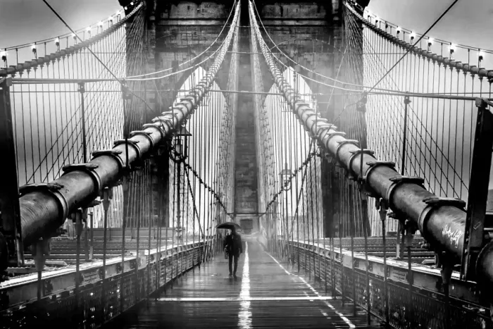 Framed Print : A lone man with umbrella walks along a foggy Brooklyn Bridge at dusk in black and white