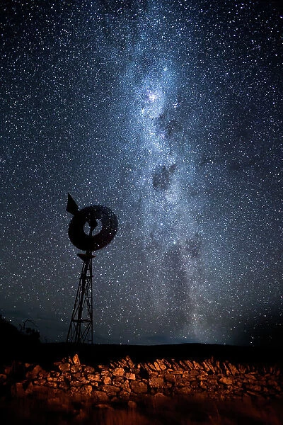 The Milky Way, stars and a clear night sky over a windmill. An old hand made stone fence in the foreground. Eyre Peninsula. South Australia