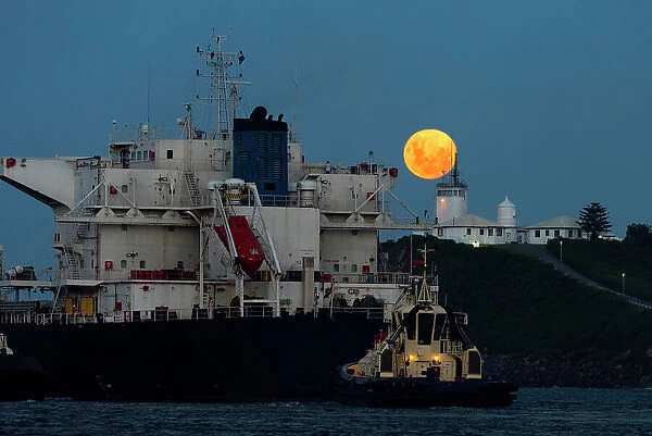 full moon rising above a lighthouse with ship in foreground