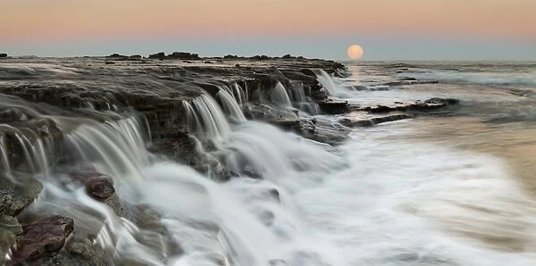 Moon rising over seascape waterfall