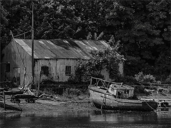 Old boatshed and derelict fishing boat moored on the river at Caernarfon, Northern Wales, United kingdom