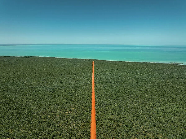 Orange coloured dirt road heading towards the Indian Ocean photographed from an aerial perspective on a sunny day, Western Australia, Australia