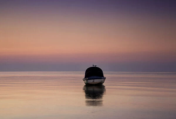 Reflections of a single boat moored on the bay at sunrise in fog, South Werribee