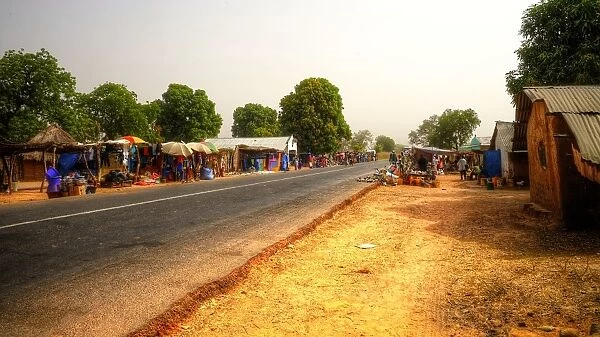 Road market in rural Gambia with colourful stalls, clear sky and no cars