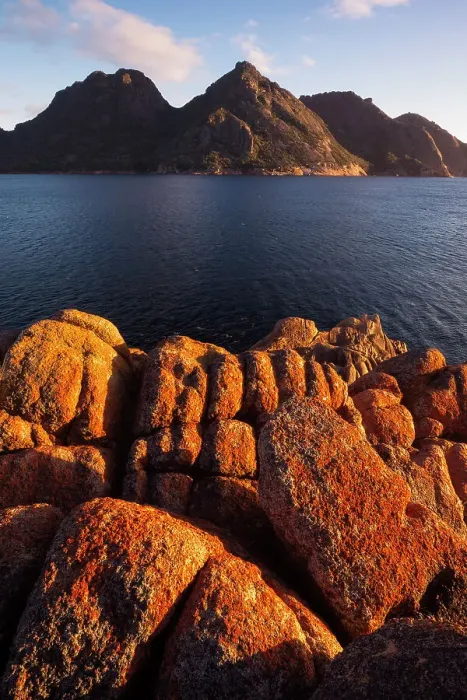 Framed Print : Sunrise at Wineglass Bay lights up lichen covered boulders with the Hazards mountain range beyond, Freycinet National Park, Tasmania, Australia