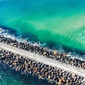 Aerial View of rock walkway out into the ocean with surfers