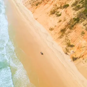 Aerial view of sand dunes with vehicles travelling along the sand and the ocean