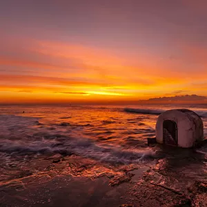 Beautiful red, yellow and orange colors of a sunrise over the ocean with a little concrete hut