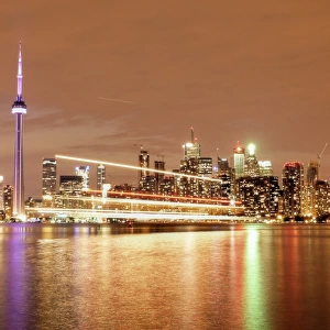 Canada, Ontario, Toronto, Illuminated waterfront skyline and CN Tower reflecting in Lake Ontario with passing ferry light trails