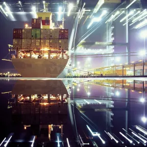 Container ship being loaded by illuminated cranes in dock, night