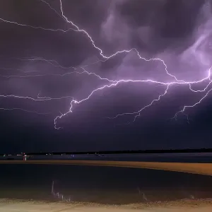 Flashes of bright lightning strikes across the water with stormy clouds and sky