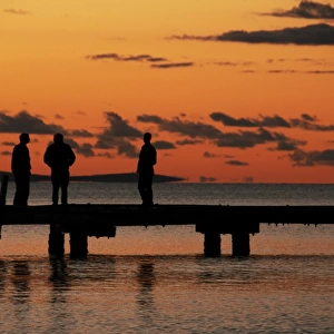 Silhouetted people on pier at sunset