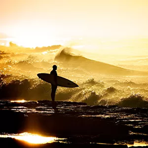 Surfer holding surfboard on rocks