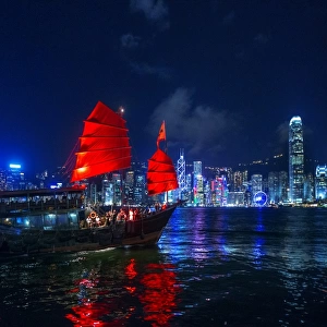 A Traditional Chinese Junk Sailing In Victoria Harbour With View of Hong Kong Island Skyline At Night, Hong Kong, China