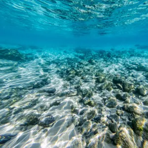 Underneath a wave in the clear ocean waters looking at rocks and shells on the ocean floor