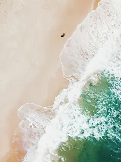 An aerial beach shot of guy walking on the beach and the waves breaking on the shore