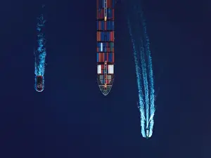 Aerial view of a cargo ship being guided by a tugboat and a pilot boat into the harbour