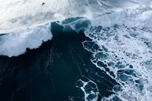 Aerial Viewpoint of a bright sunrise and deep blue ocean waters with people surfing